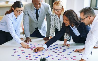 Diverse group of smiling businesspeople working together around a boardroom table in an office trying to solve a jigsaw puzzle