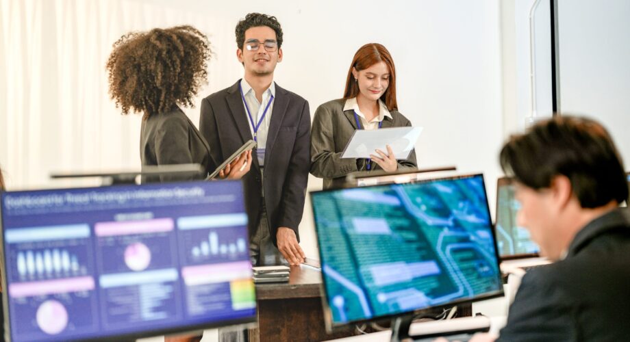Multiethnic AI security squad analyzing threat intelligence in a bright SOC. Diverse IT experts collaborating on machine learning defense behind blurred data dashboards.