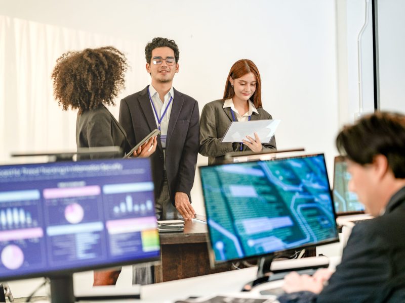 Multiethnic AI security squad analyzing threat intelligence in a bright SOC. Diverse IT experts collaborating on machine learning defense behind blurred data dashboards.