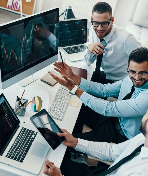 Achieving best results together. Top view of young modern men in formalwear analyzing stock market data and smiling while working in the office