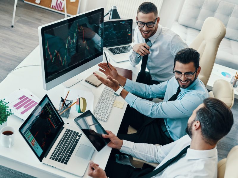 Achieving best results together. Top view of young modern men in formalwear analyzing stock market data and smiling while working in the office