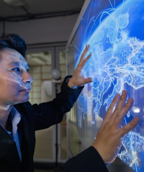A professional man interacts with a high-tech circular data interface on a large digital screen, featuring graphs and data elements in a glowing blue theme.