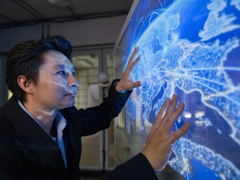 A professional man interacts with a high-tech circular data interface on a large digital screen, featuring graphs and data elements in a glowing blue theme.
