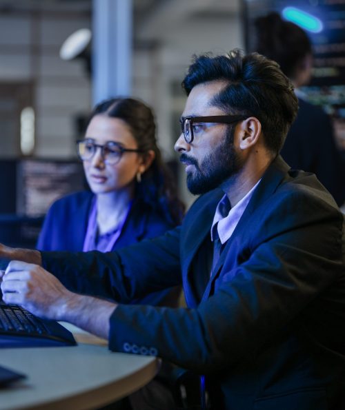 A diverse team of AI developers shares a successful moment in the office. A female programmer smiles as they review the positive results of a complex machine learning algorithm.