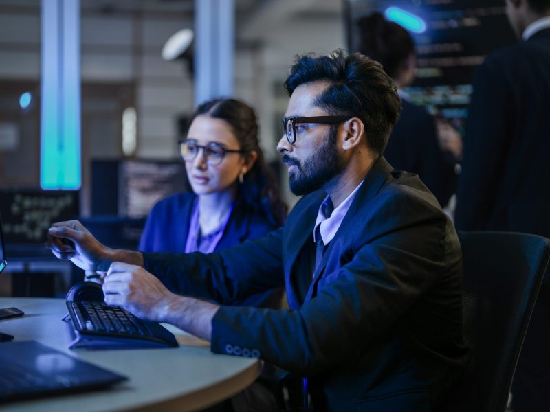 A diverse team of AI developers shares a successful moment in the office. A female programmer smiles as they review the positive results of a complex machine learning algorithm.