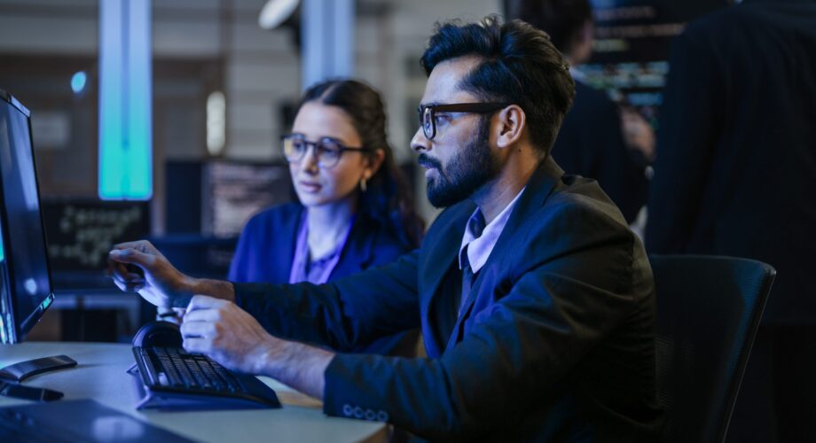 A diverse team of AI developers shares a successful moment in the office. A female programmer smiles as they review the positive results of a complex machine learning algorithm.